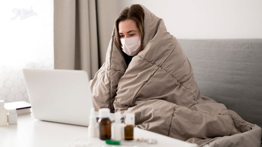 Woman wrapped in a blanket wearing a face mask using a laptop, medicine bottles on the table — 10個簡單習慣提升免疫力 · 10 simple daily habits to support immunity