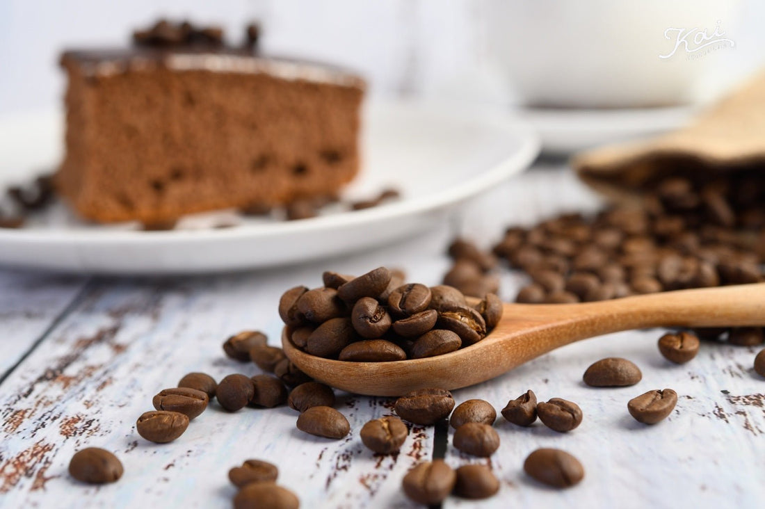Wooden spoon overflowing with roasted coffee beans on a rustic table, chocolate cake in the background — 康普茶的低咖啡因秘密 · The low-caffeine secret behind kombucha